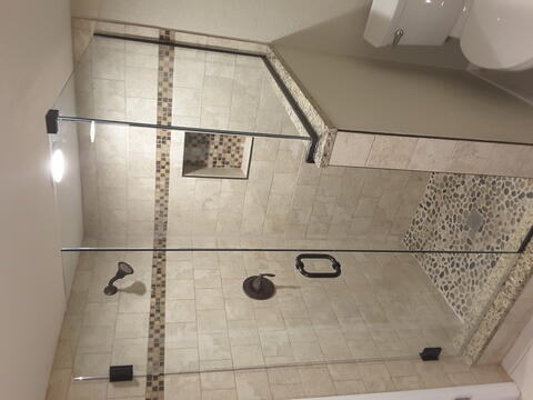 A beige tiled shower with a half wall on one side and a custom frameless glass shower enclosure from Glass Doctor of Sarasota.