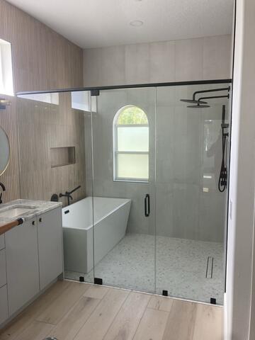 A wet room bathroom with a tub and shower behind a semi-frameless straight glass enclosure with black hardware by Glass Doctor of Sarasota.