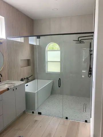 Custom glass with a center door and black hardware on a wet room with tub and shower installed by Glass Doctor of Tampa Bay