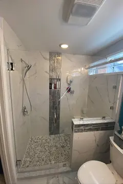 A custom walk-in shower with gray tile and a frameless glass swing door by Glass Doctor of Raleigh
