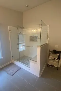 A shower with white tile, a swinging glass door, and frameless glass panels on two sides with brushed nickel hardware