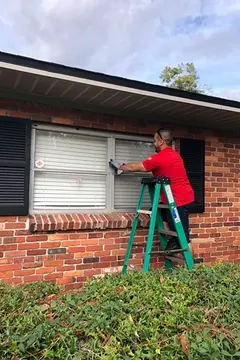 A Glass Doctor of Tampa Bay service professional standing on a ladder and repairing the window of a house. 