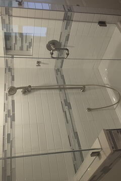 Angle one of a frameless glass shower door installed on a tub with white subway tiles and gray accent tiles by Glass Doctor of Sarasota.