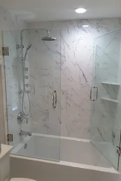 A frameless glass shower swinging door installed on a tub with white marbled tile by Glass Doctor of Tampa Bay.