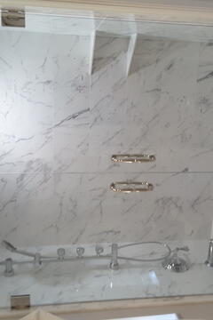 A tub with marbled walls and a frameless glass double-door enclosure and chrome hardware by Glass Doctor of Pinellas County.